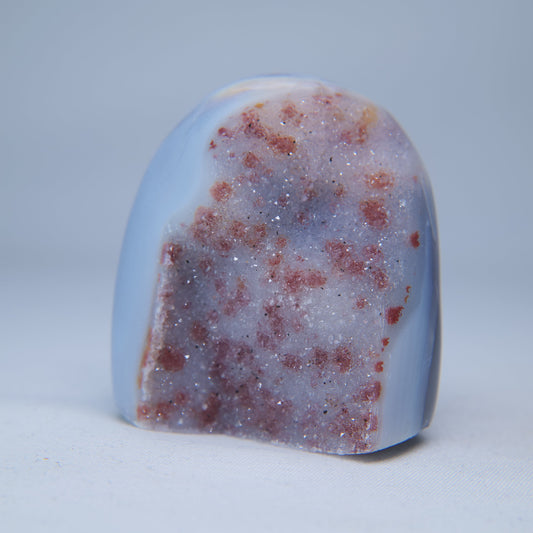 Front view of the pale-pink druzy face, dotted with red-pink inclusions and edged in blue agate.