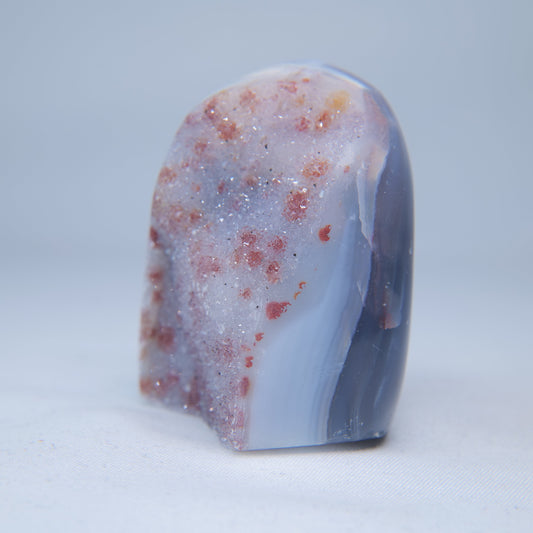 Angled view of red-pink inclusions across the glittering druzy surface and blue-grey side. alternate view