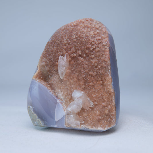 Peach-orange druzy agate freeform, front view with clear quartz accents and a lavender-grey polished base.