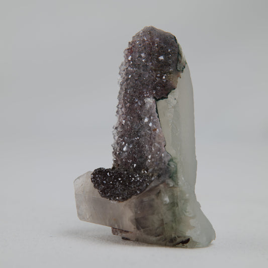 Side profile of the druzy, showing lavender-grey crystals draped over a pale blocky base with a green-tinted edge. alternate view